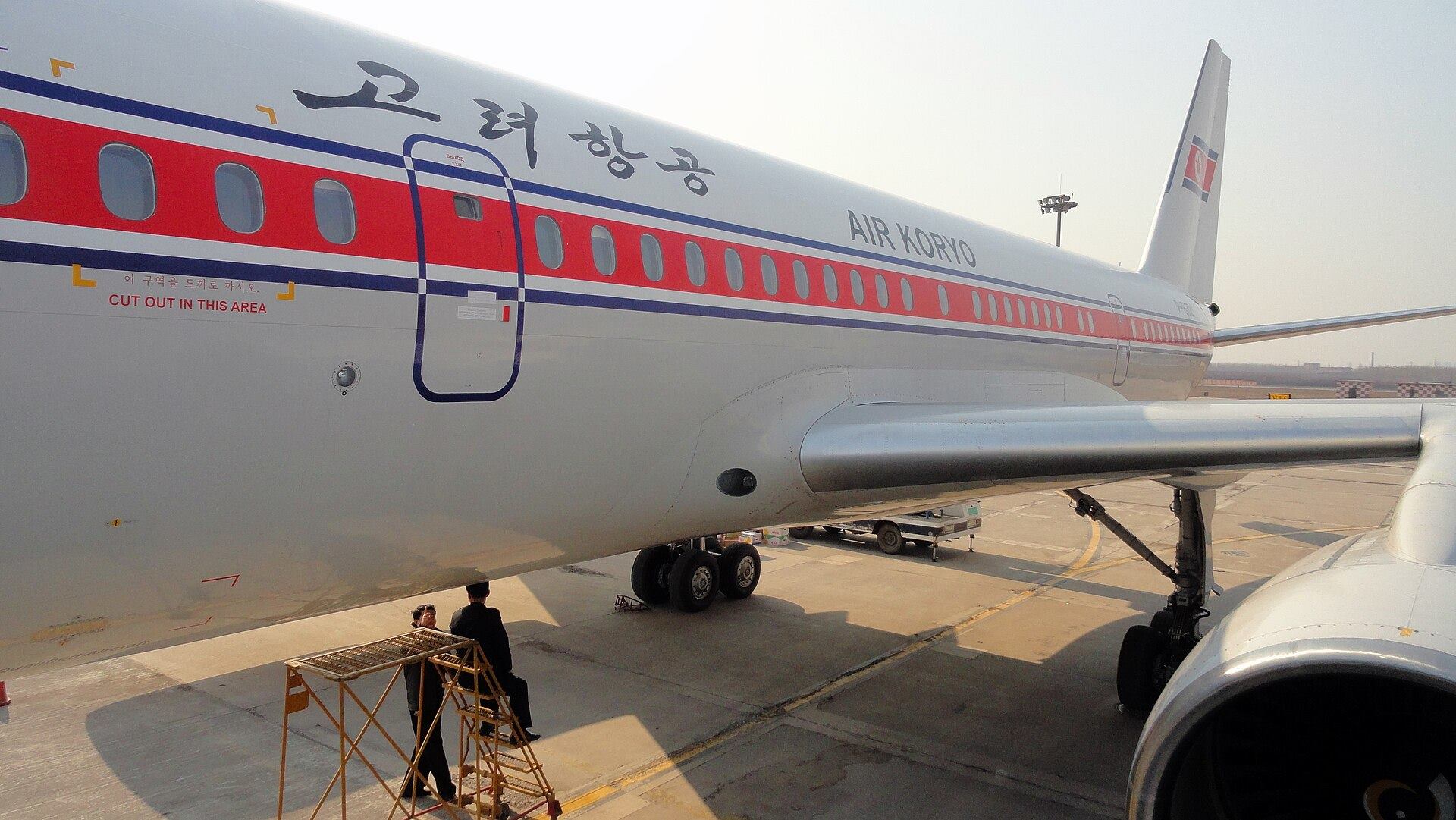 A white airliner with red stripes and Korean lettering parked on the apron, with a ground crew member by the engine.