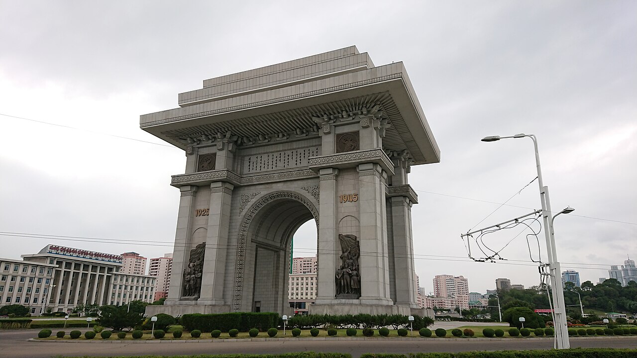 The Arch of Triumph in Pyongyang, a huge stone arch on a wide road under a cloudy sky.