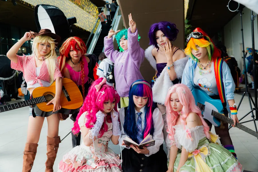 A large group of colourfully dressed cosplayers posing together with a guitar.