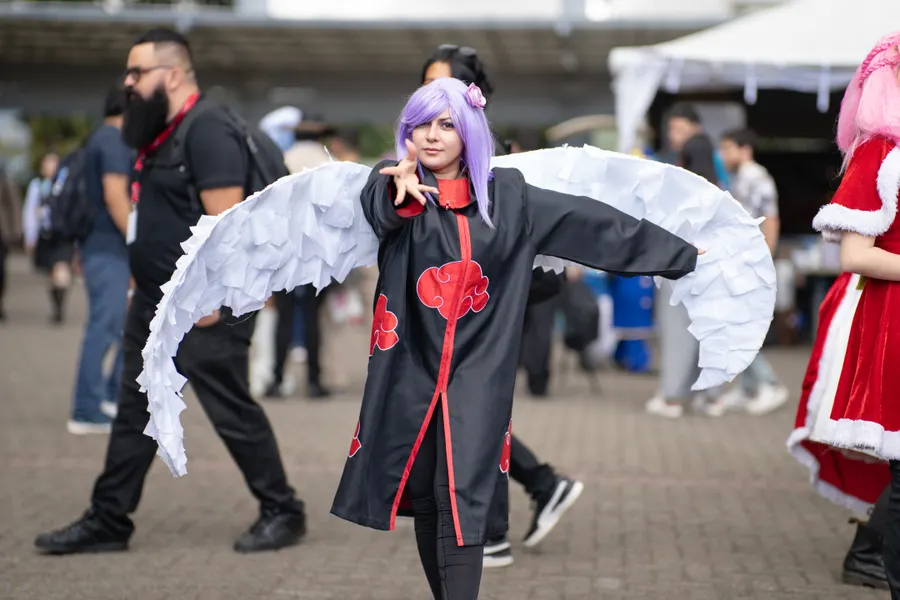 A cosplayer with large white feathered wings posing in a convention crowd.