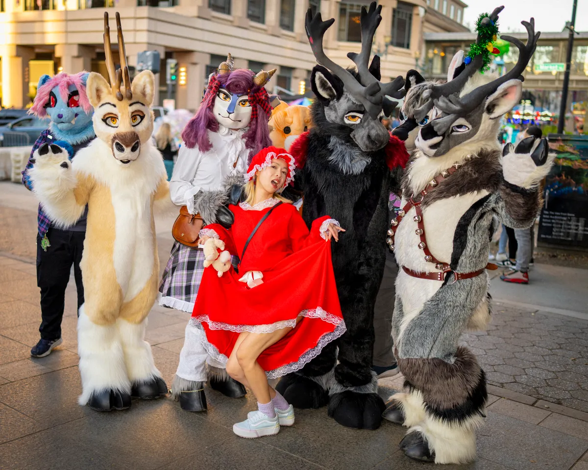 A group of people in colourful animal fursuits posing together in a town square.