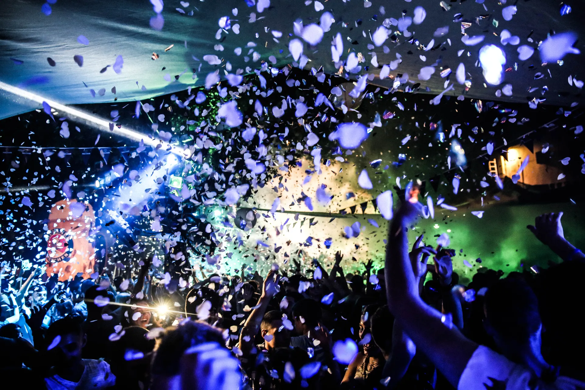 Confetti raining down over a crowd with raised hands under blue and green stage lights.