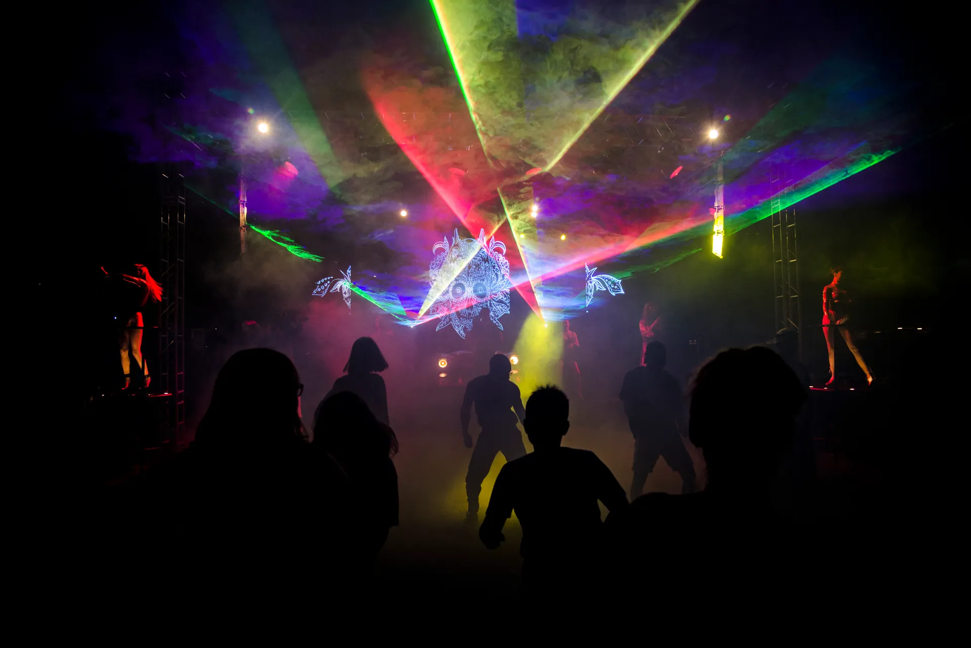 Silhouettes dancing under colourful laser beams in a dark hall.