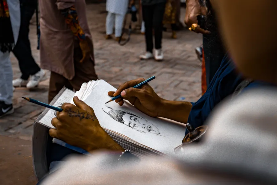 An artist's hands sketching a portrait in pencil in a notebook.